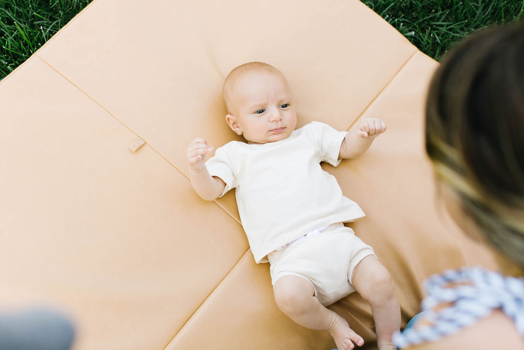 baby laying on a toki mats play mat and looking up at mom