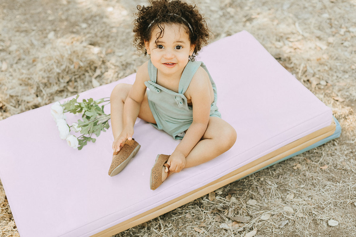 toddler sitting on stacked up toki mats play mats outside
