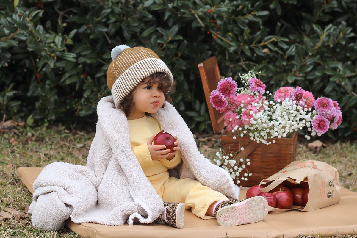 baby sitting on a toki mats play mat outside next to flowers and fruit