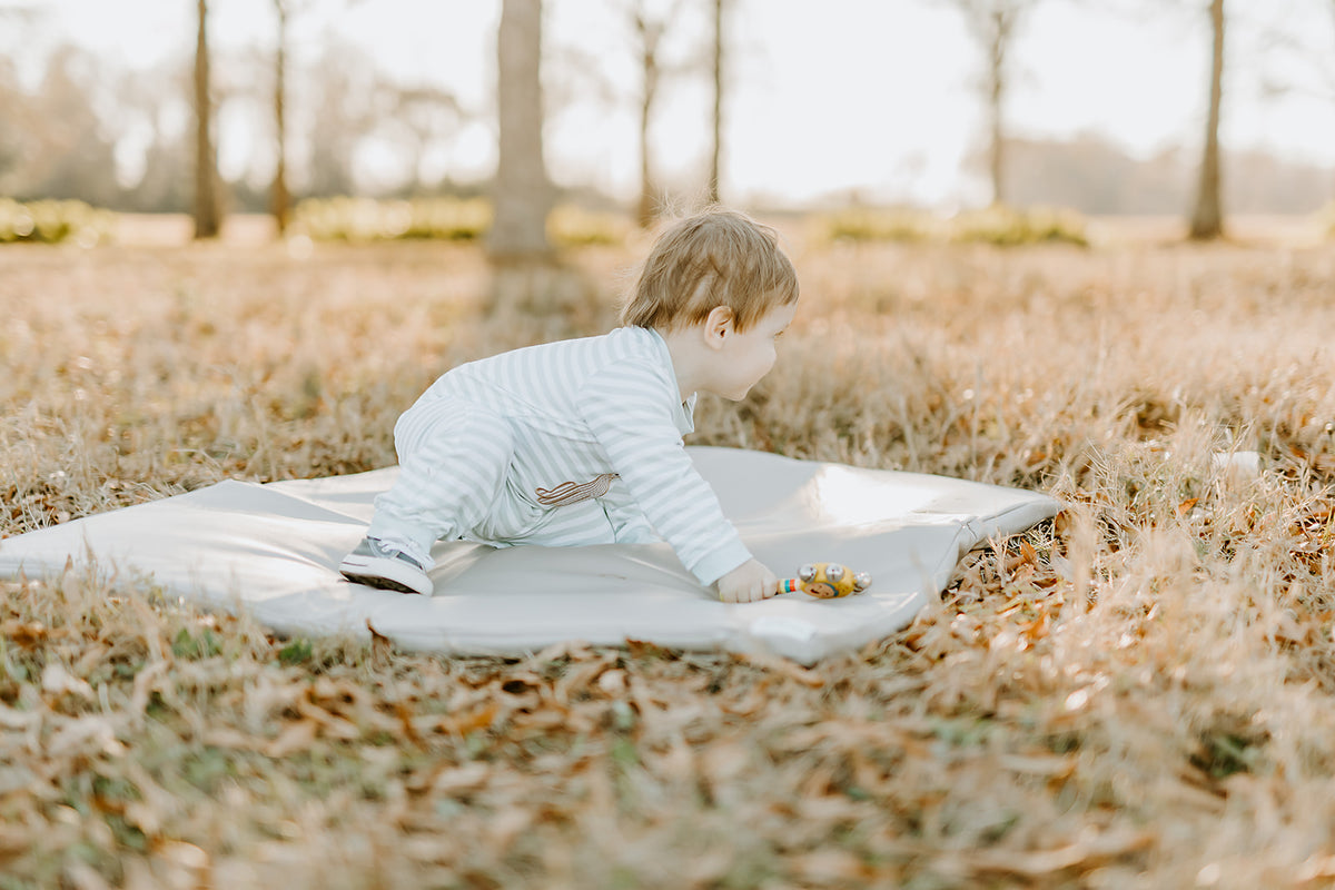 baby crawling on a toki mats padded play mat outdoors in a grassy area