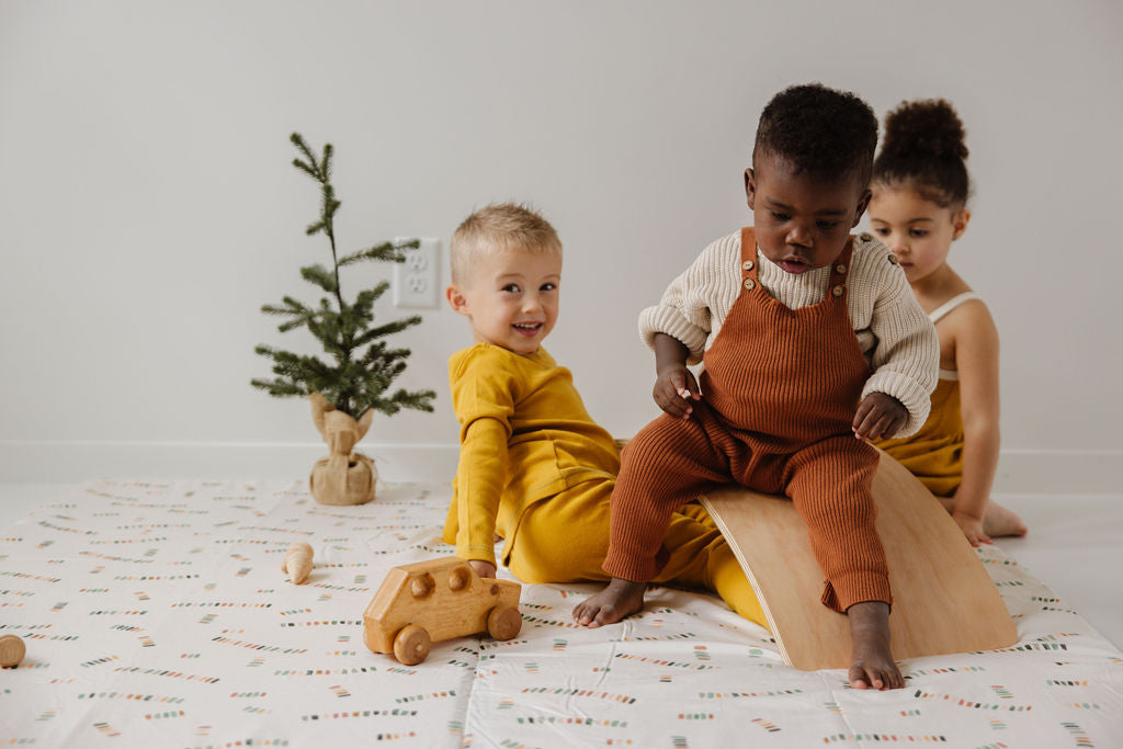 kids playing on a toki mat with wooden toys and a small fir tree