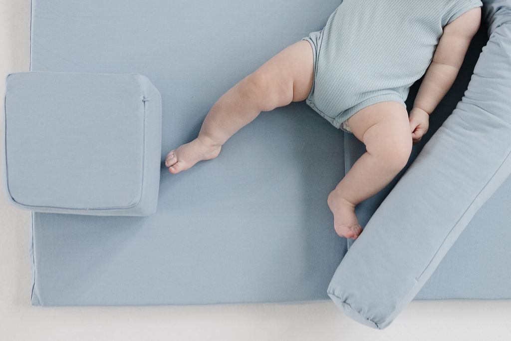 baby laying on a toki mats play mat with a play cube and a support pillow