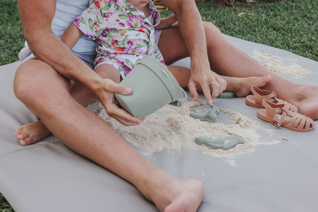 parent and child playing with sand on a toki mats vegan leather mat