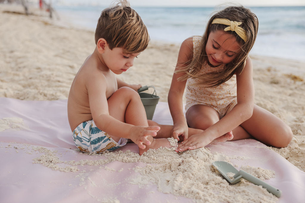 two kids playing on a toki mat at the beach