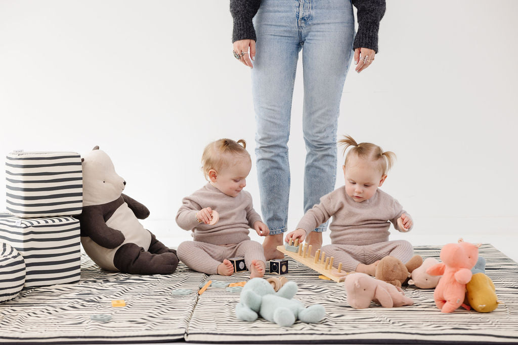 babies playing on a toki mats play mat with an adult standing up behind them