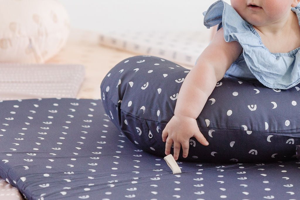 baby laying on a toki mat and a nursing pillow