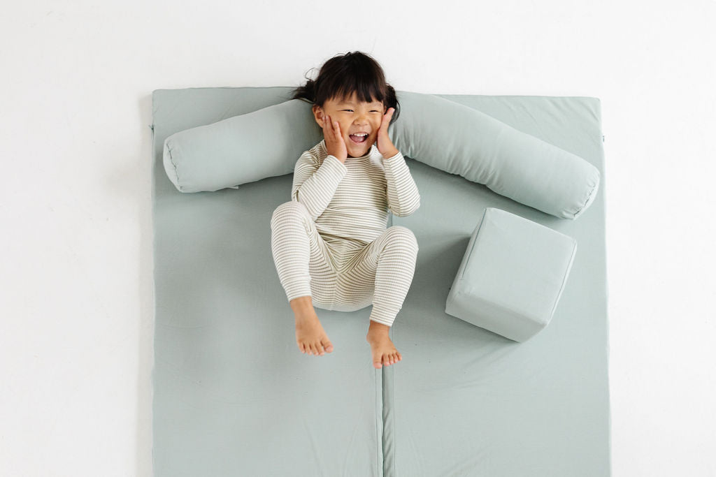 toddler laying on a toki mats play mat and support pillow
