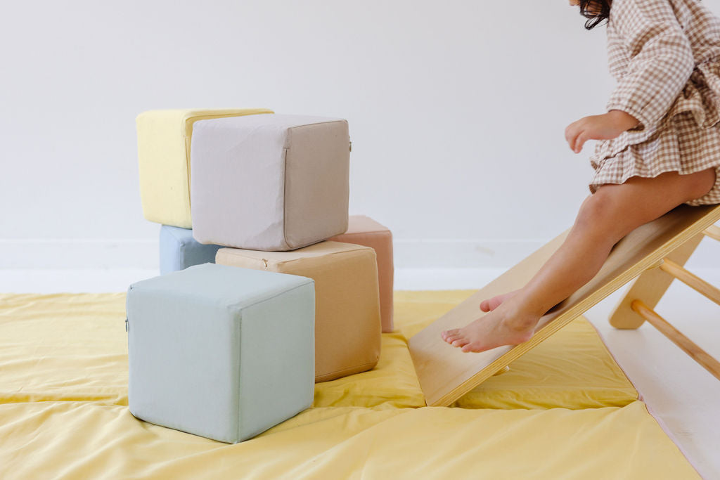 toddler sliding down a pikler onto a toki mats play mat with play cubes