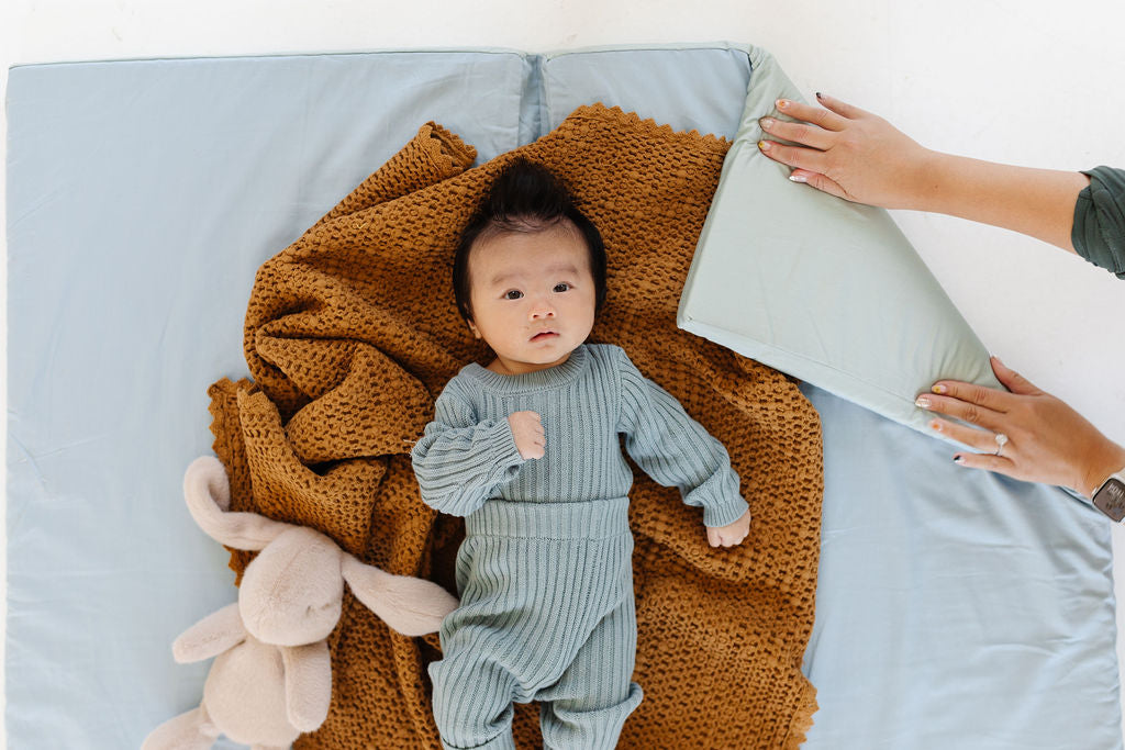 baby laying on a toki mats play mat with a blanket and a stuffed animal