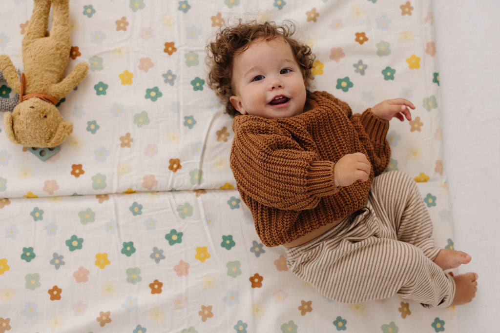 baby laying on a toki mats play mat with playful posies print